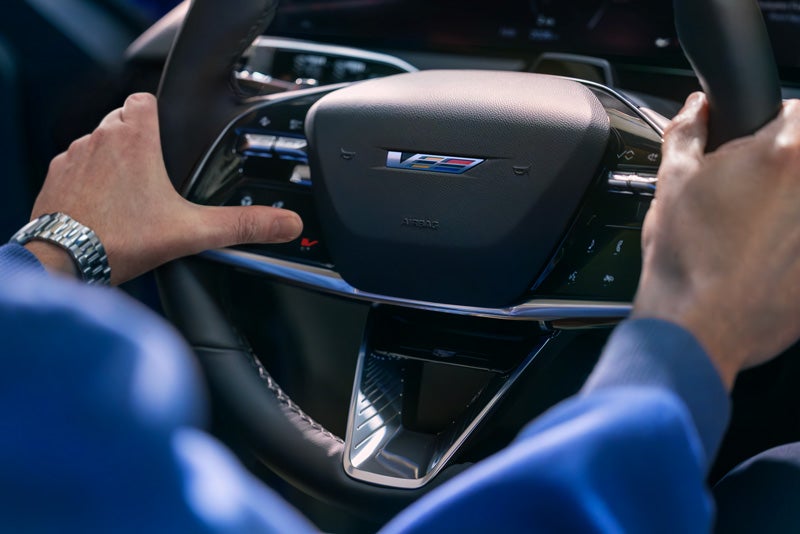 Close-up of a Man About to Press the V-Button on the 2026 OPTIQ-V Steering Wheel | Baldwin Cadillac in POPLAR BLUFF MO